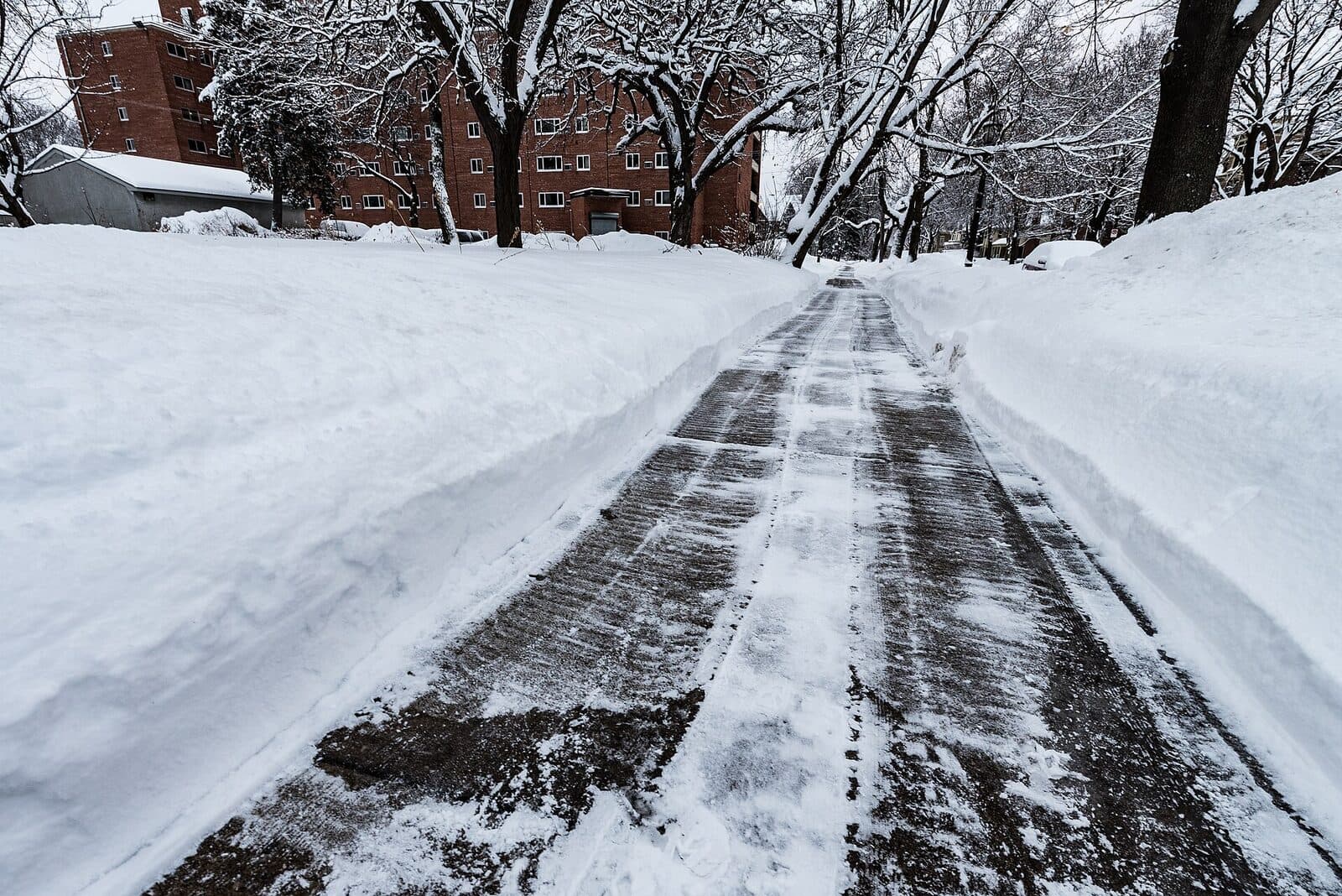 A homeowner shovels snow from a sidewalk in front of a suburban home